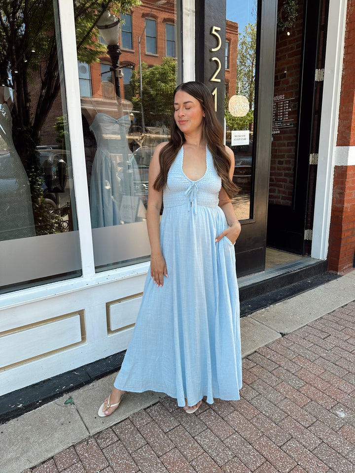 Woman wearing blue smocked midi dress with halter neck, tie detail, and pockets.
