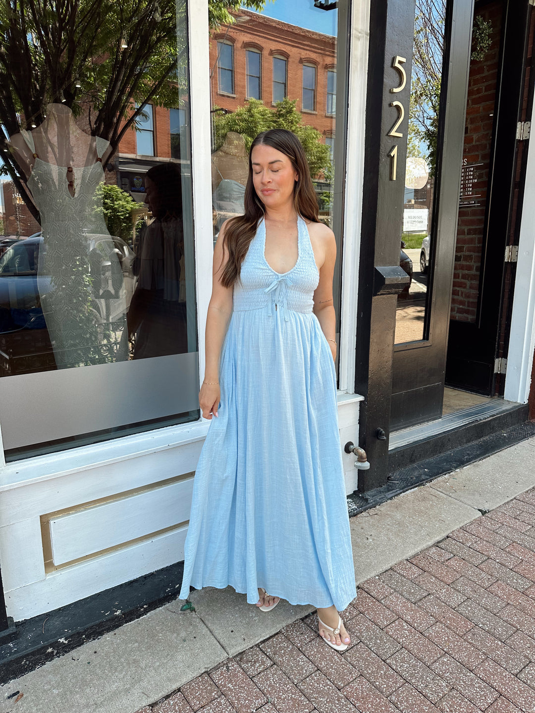 Woman wearing blue smocked midi dress with halter neck, tie detail, and pockets.