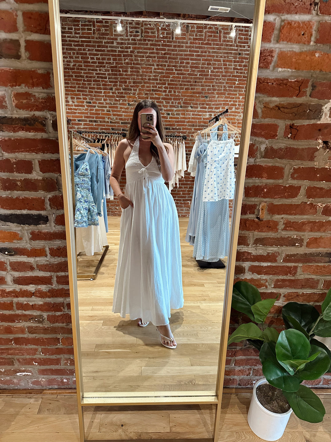 Woman wearing white smocked midi dress with a halter neck, tie detail, and pockets.