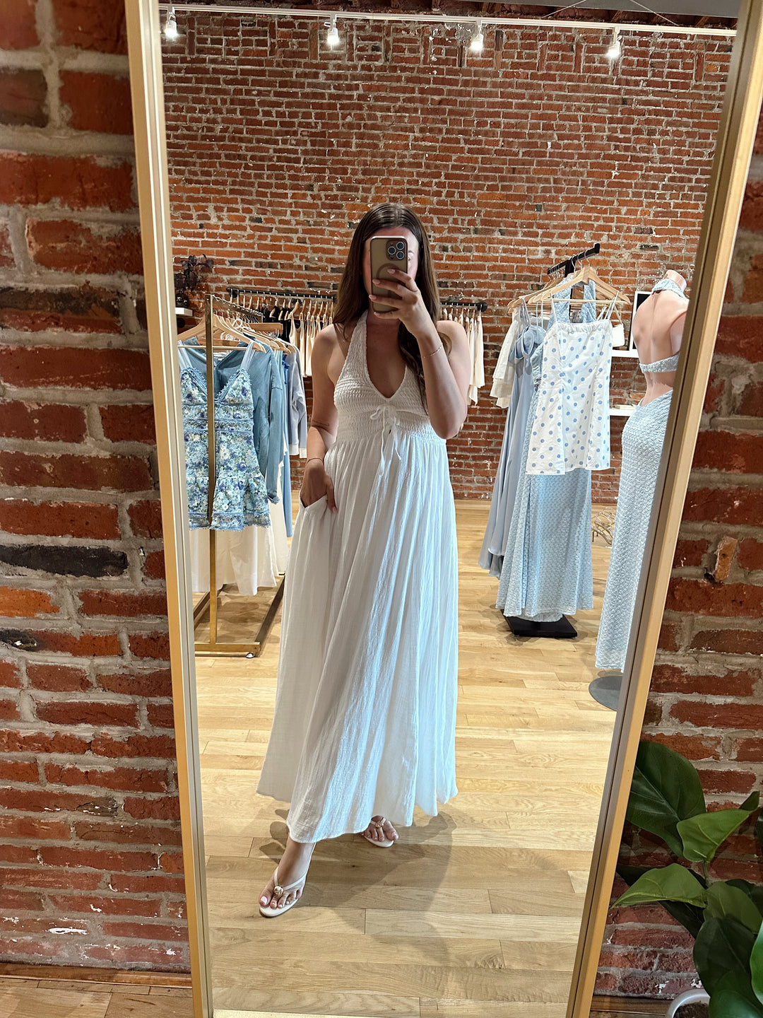 Woman wearing white smocked midi dress with a halter neck, tie detail, and pockets.