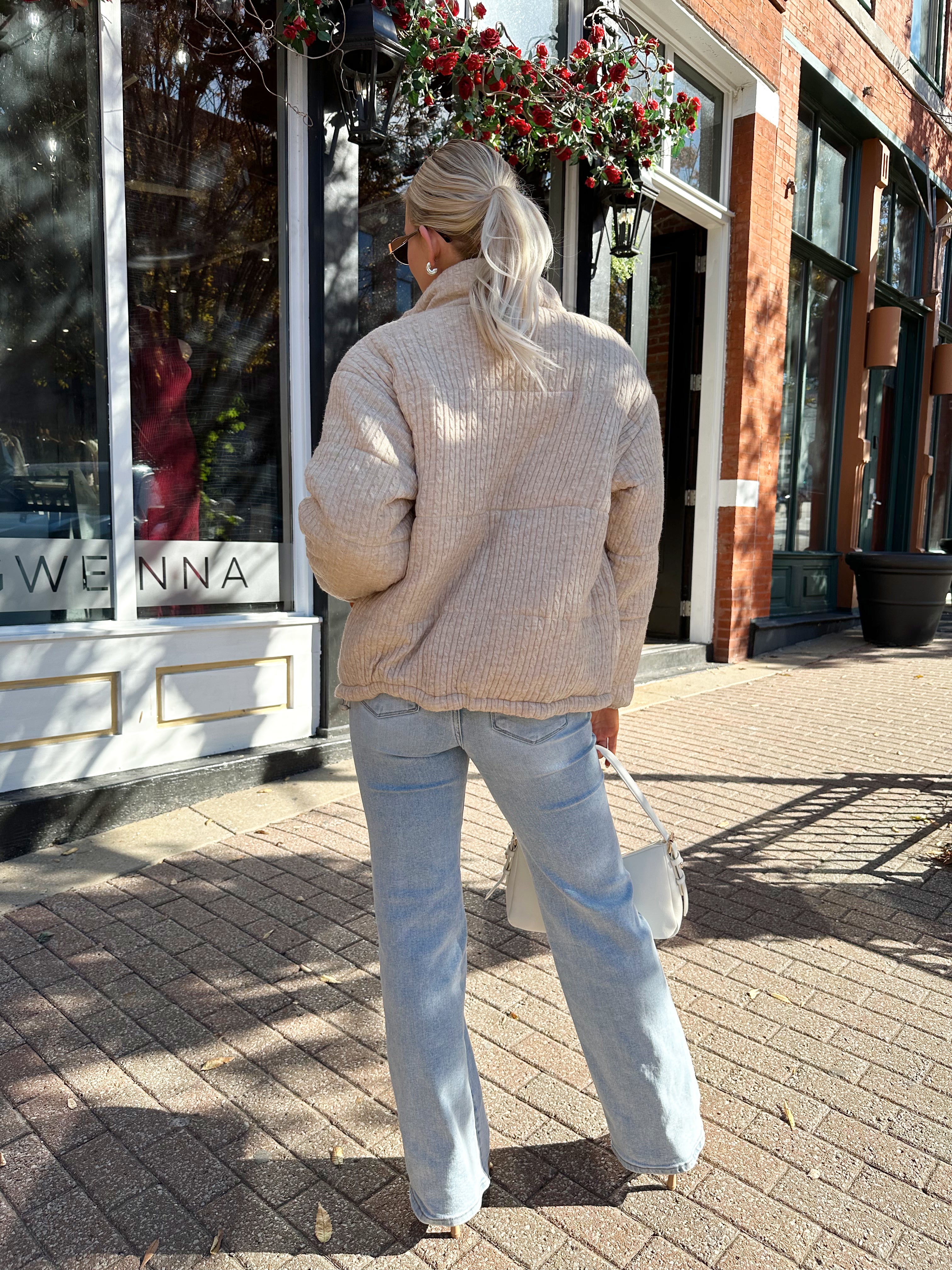Woman wearing beige cable knit puff coat with light wash jean.