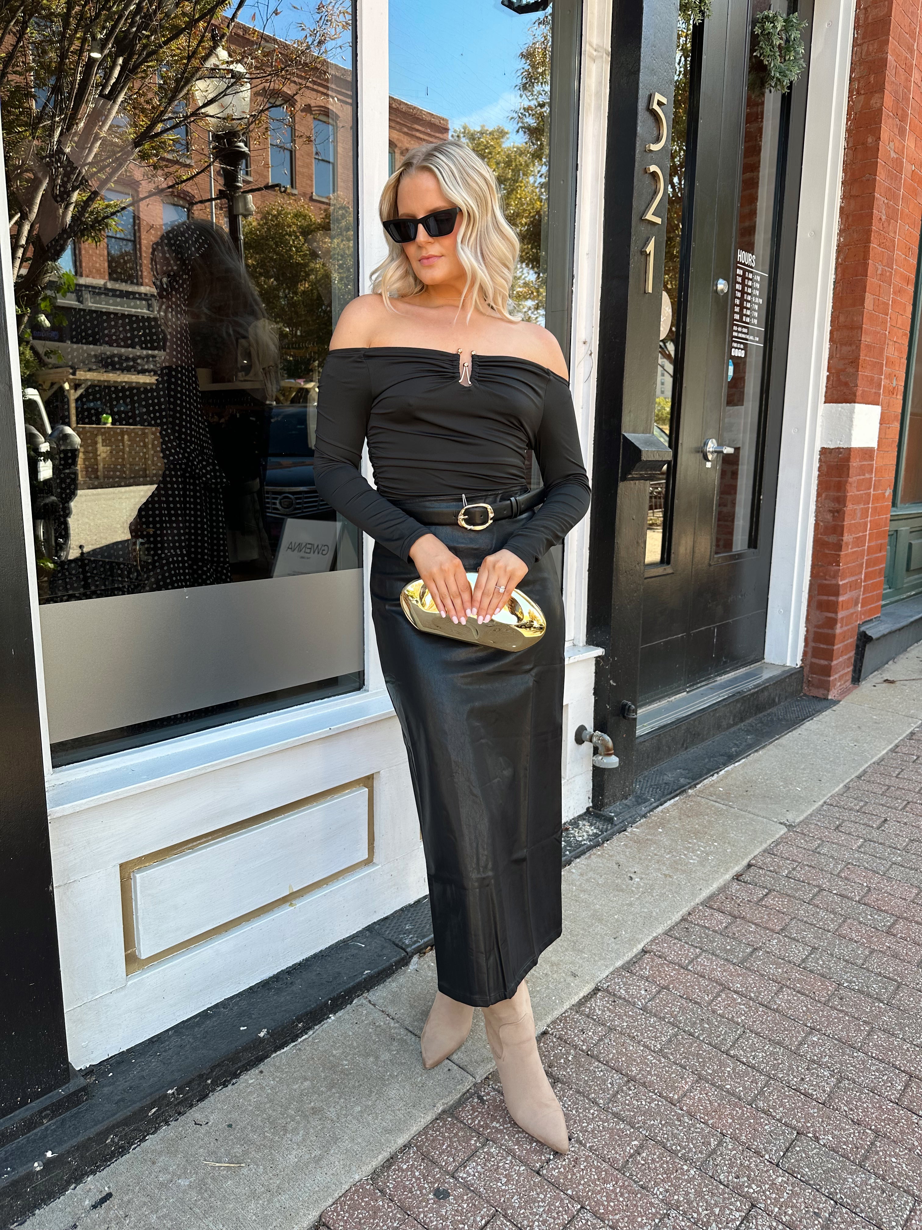 Woman wearing black long sleeve off the shoulder top with gold detailing. 