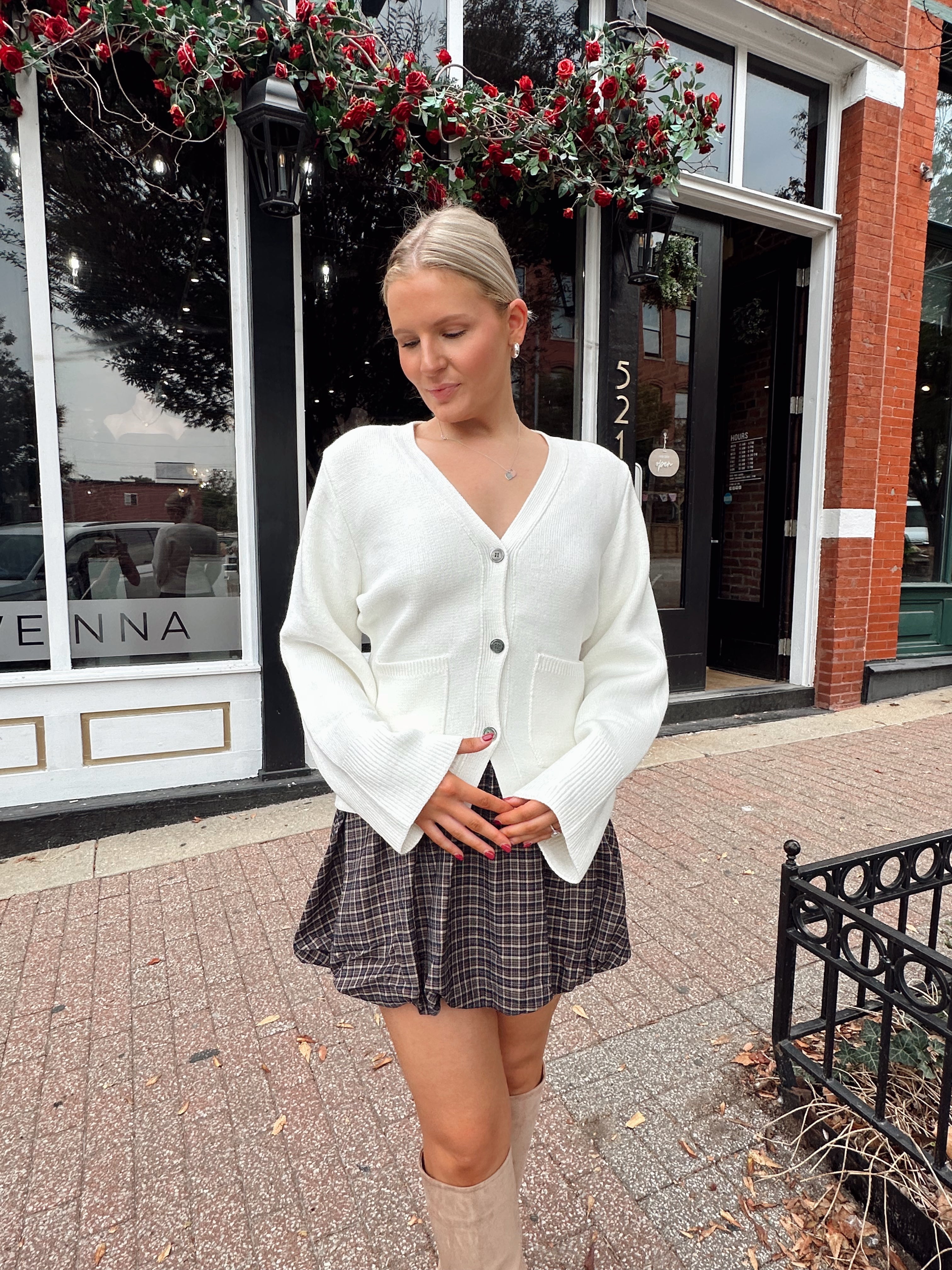 Woman wearing white fitted button down cardigan over plaid mini dress. 