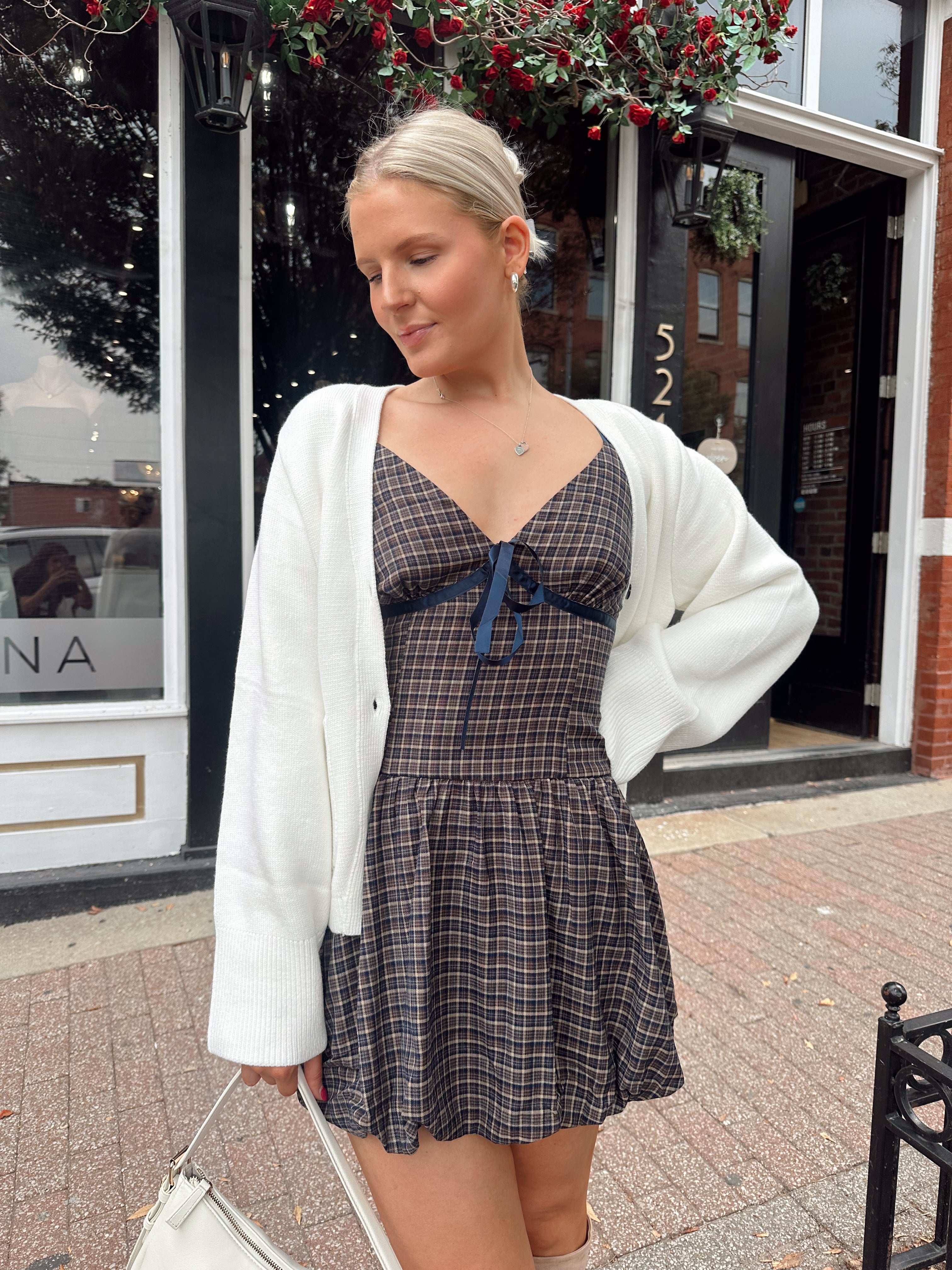 Woman wearing white fitted button down cardigan over plaid mini dress. 