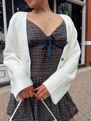 Woman wearing white fitted button down cardigan over plaid mini dress. 