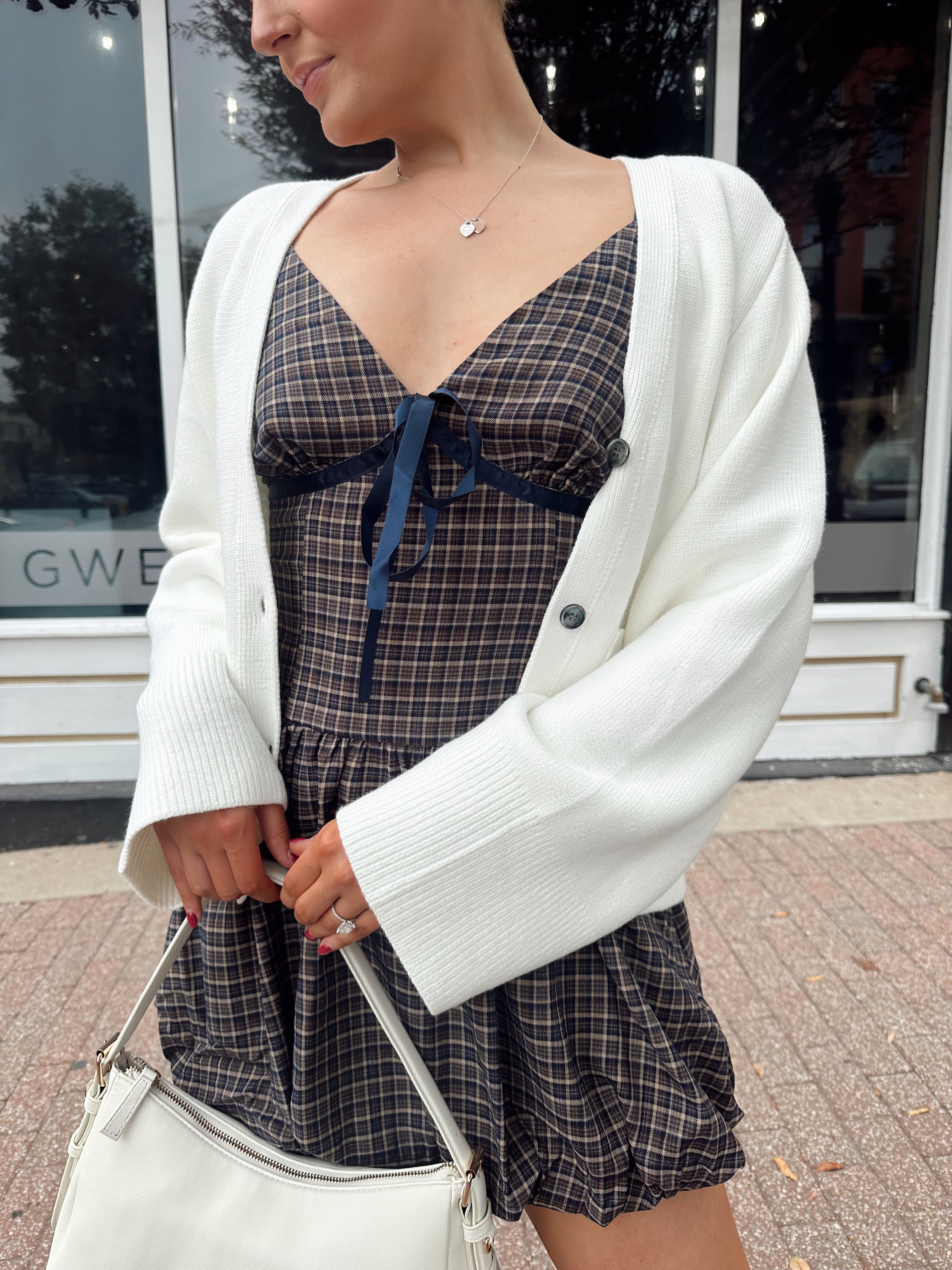 Woman wearing white fitted button down cardigan over plaid mini dress. 