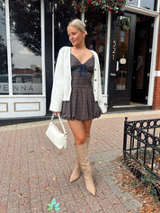 Woman wearing white fitted button down cardigan over plaid mini dress. 
