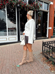 Woman wearing white fitted button down cardigan over plaid mini dress. 