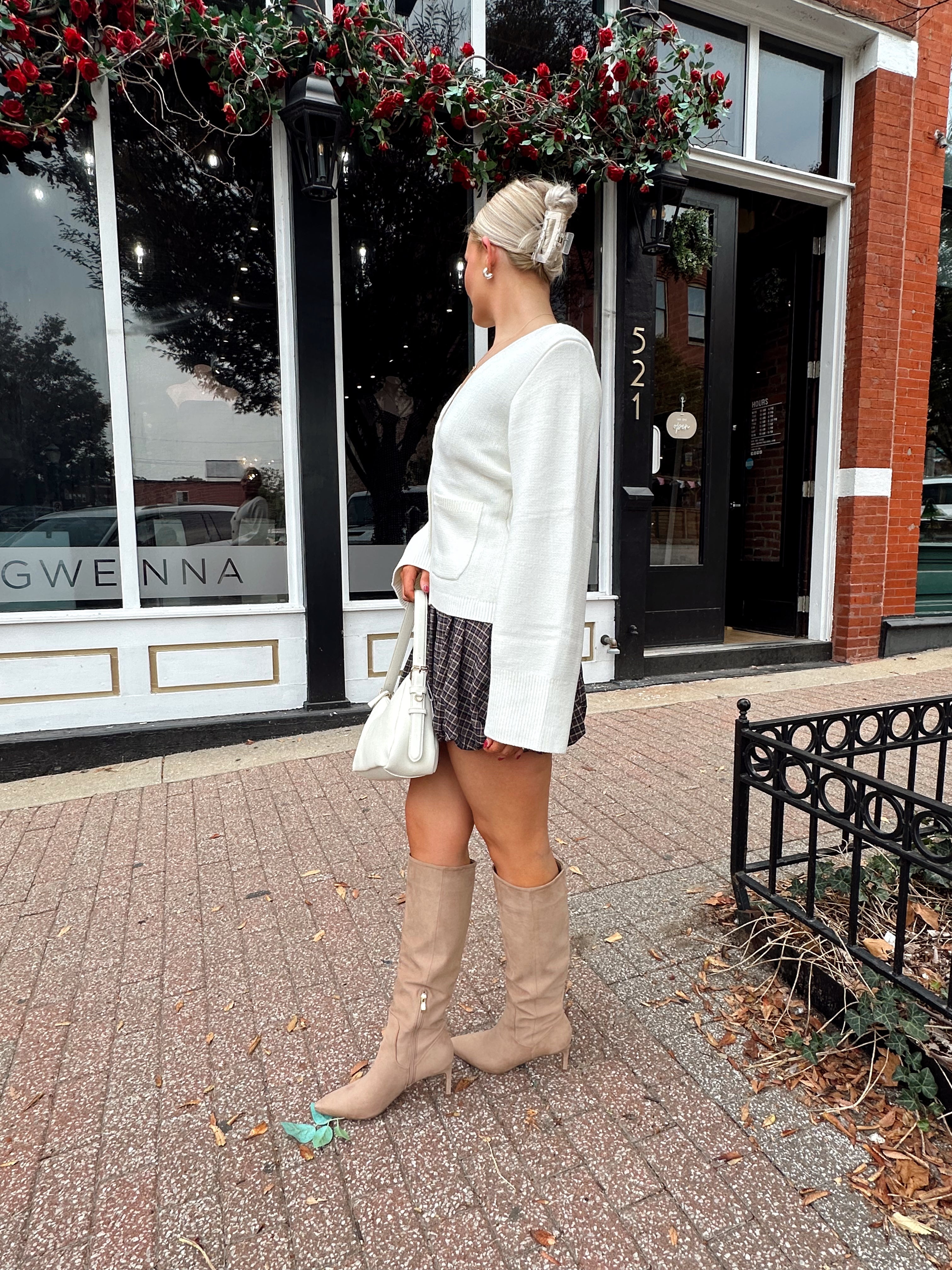 Woman wearing white fitted button down cardigan over plaid mini dress. 