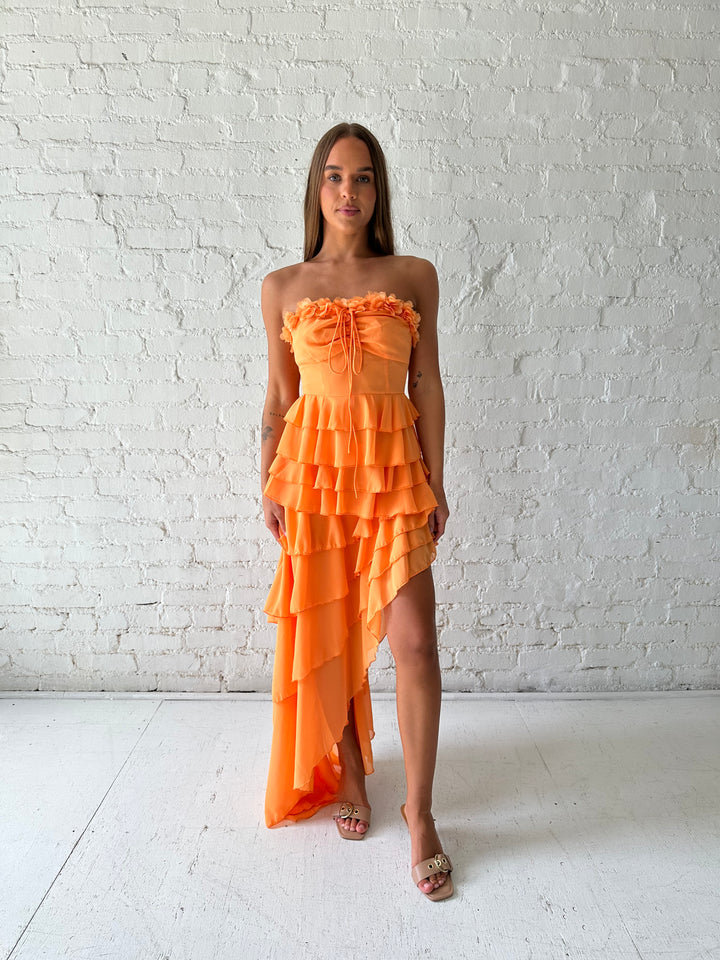 Woman wearing orange ruffle maxi dress with high-low slit. 