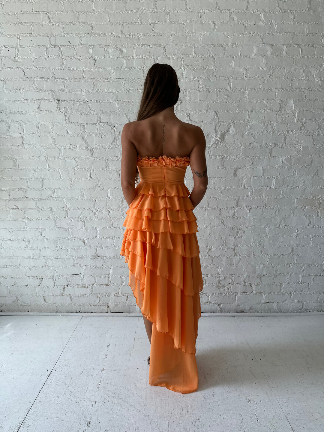 Woman wearing orange ruffle maxi dress with high-low slit. 