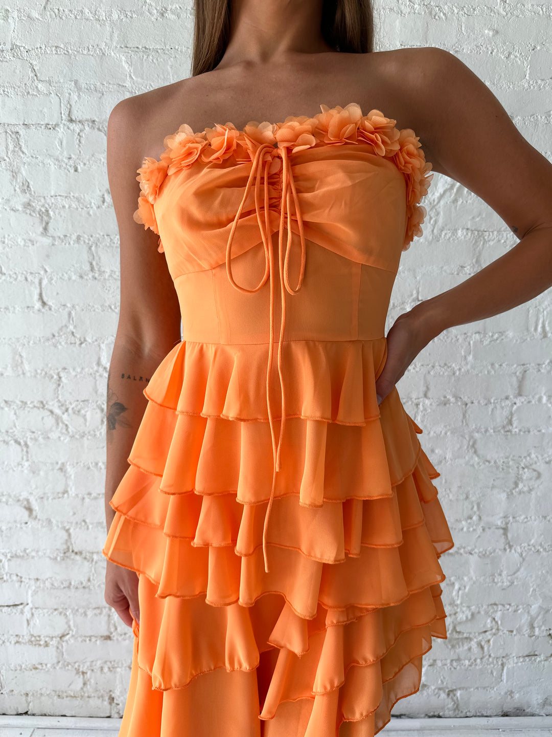 Woman wearing orange ruffle maxi dress with high-low slit. 