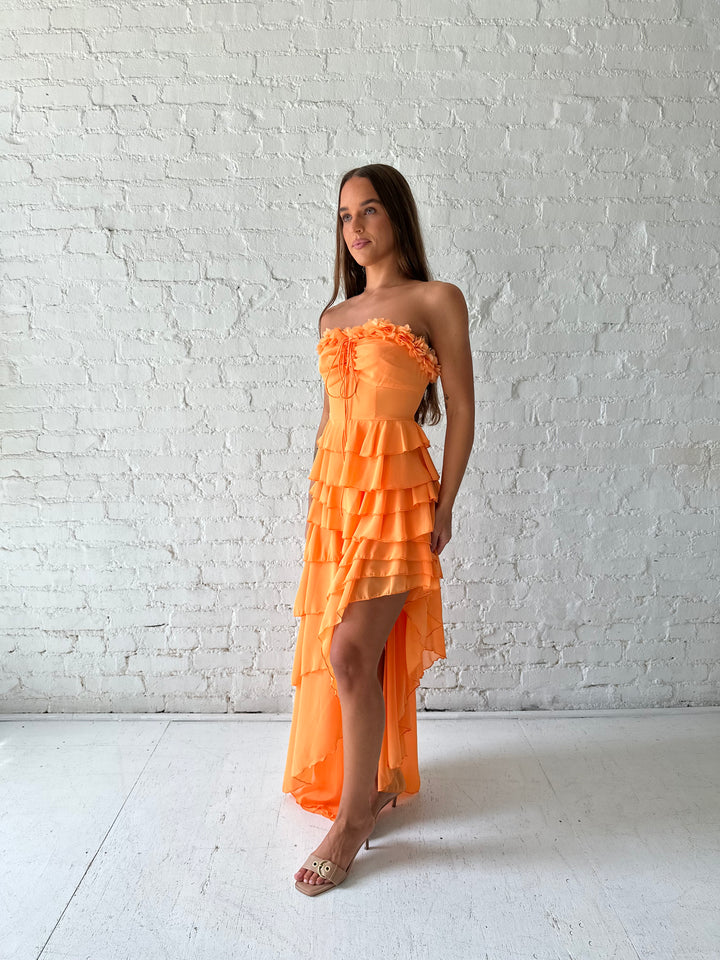 Woman wearing orange ruffle maxi dress with high-low slit. 