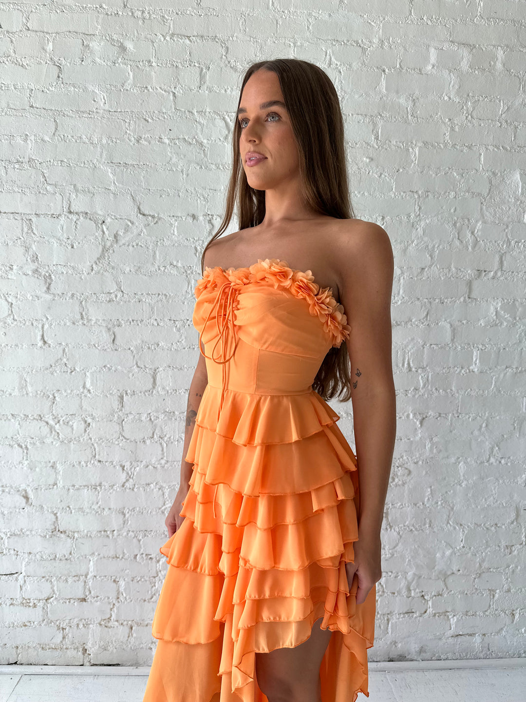 Woman wearing orange ruffle maxi dress with high-low slit. 
