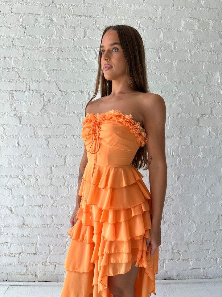 Woman wearing orange ruffle maxi dress with high-low slit. 
