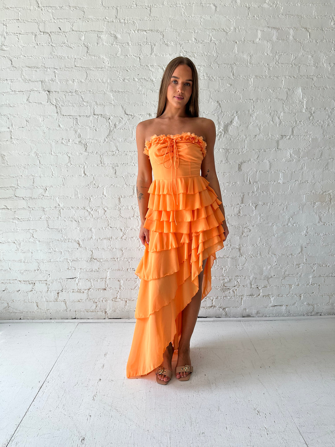Woman wearing orange ruffle maxi dress with high-low slit. 