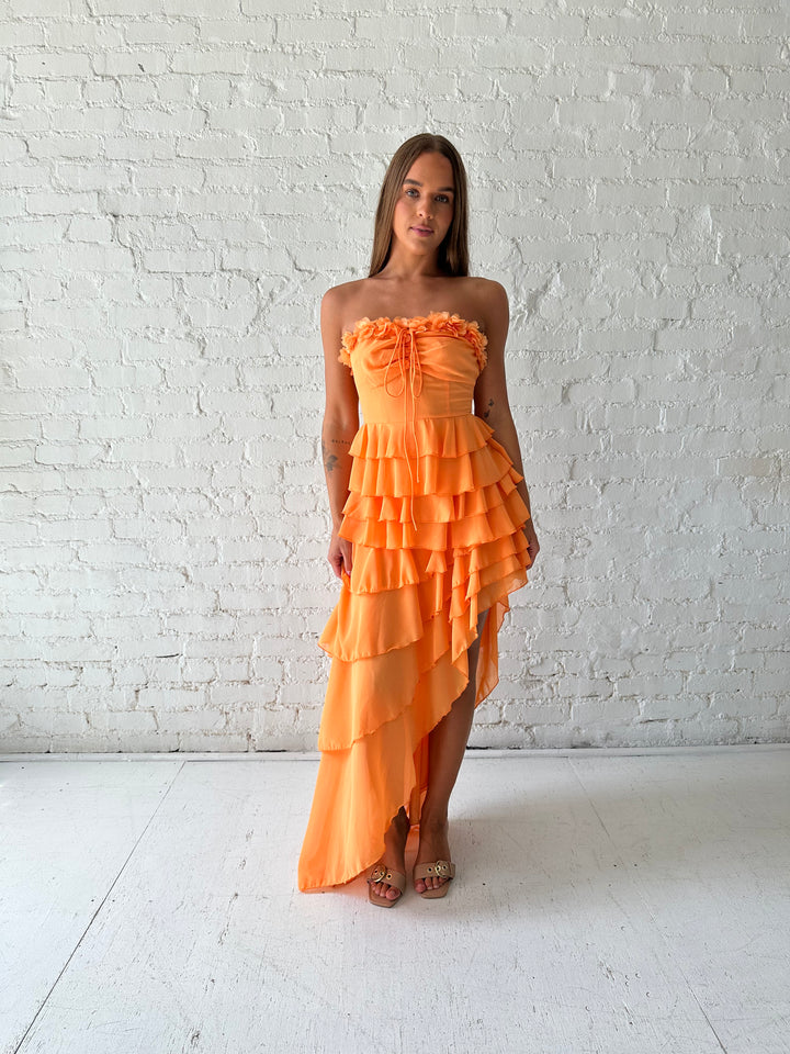 Woman wearing orange ruffle maxi dress with high-low slit. 