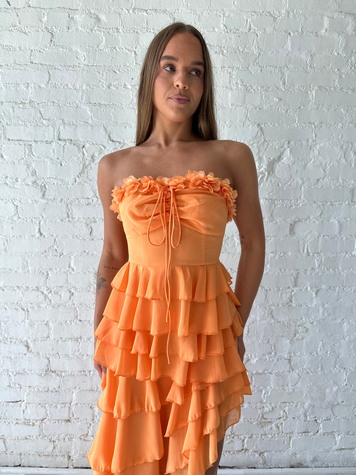 Woman wearing orange ruffle maxi dress with high-low slit. 