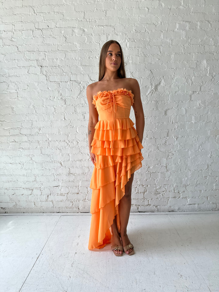 Woman wearing orange ruffle maxi dress with high-low slit. 
