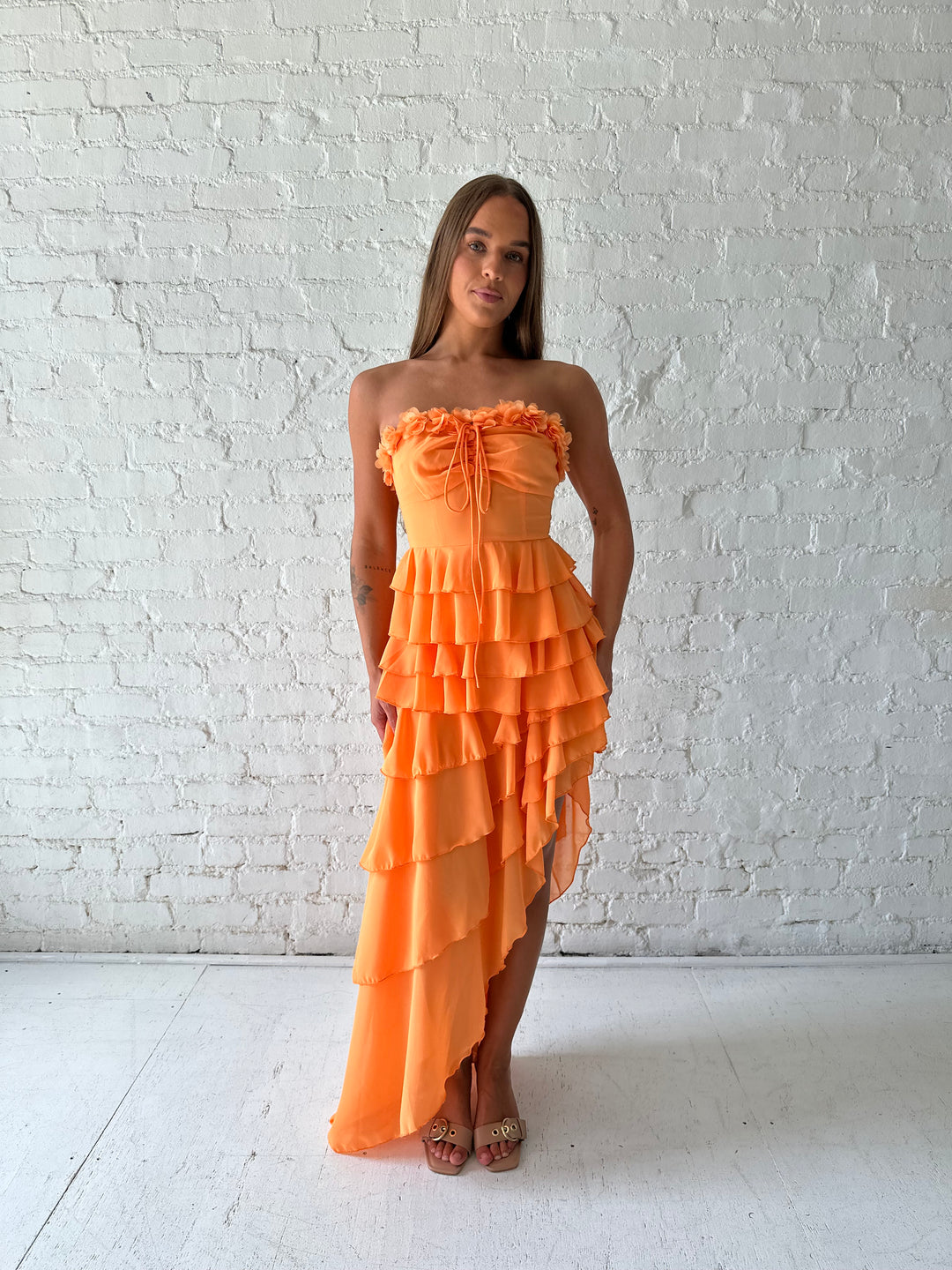 Woman wearing orange ruffle maxi dress with high-low slit. 