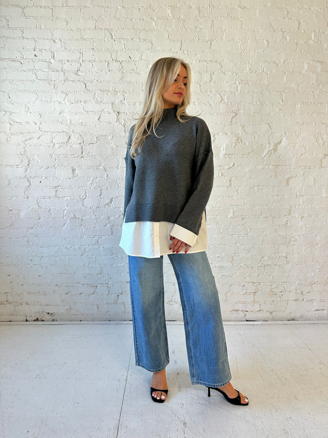 Woman wearing dark grey contrast sweater with white material sticking out the bottom.