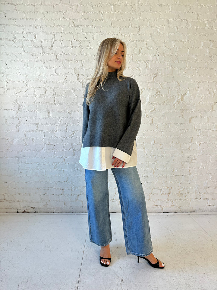 Woman wearing dark grey contrast sweater with white material sticking out the bottom.