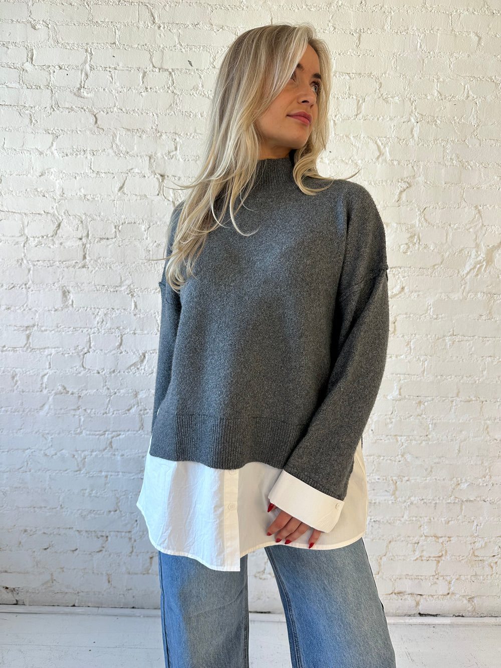 Woman wearing dark grey contrast sweater with white material sticking out the bottom.