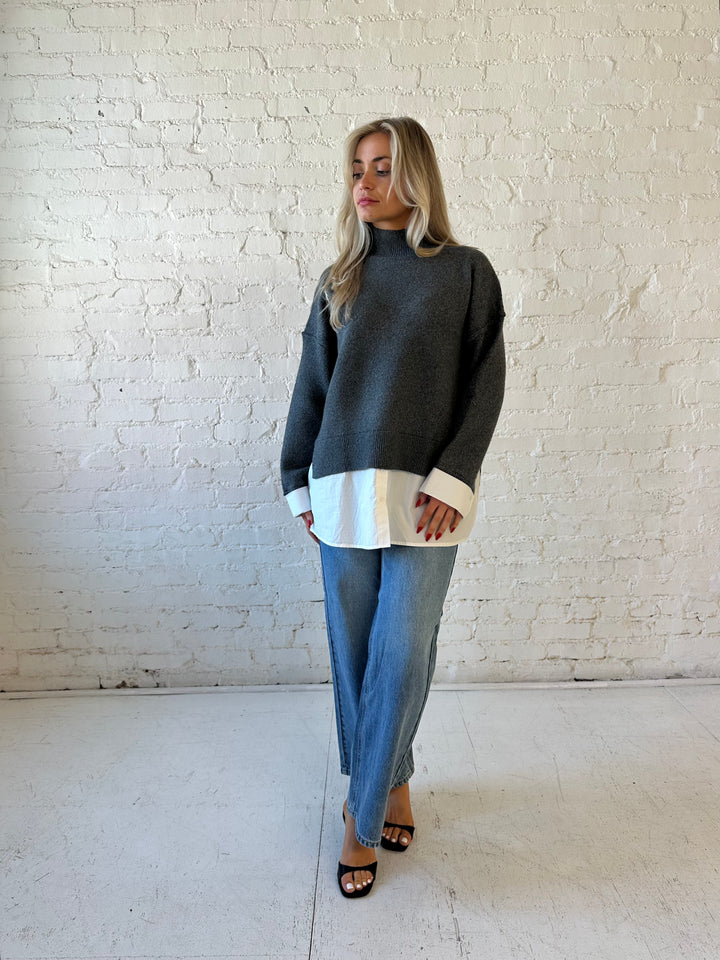 Woman wearing dark grey contrast sweater with white material sticking out the bottom.