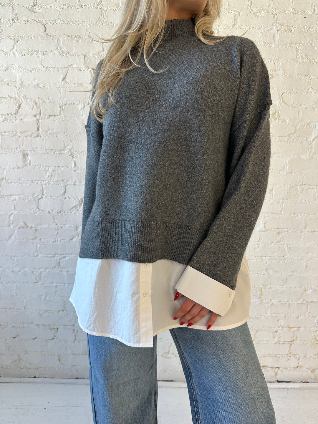 Woman wearing dark grey contrast sweater with white material sticking out the bottom.