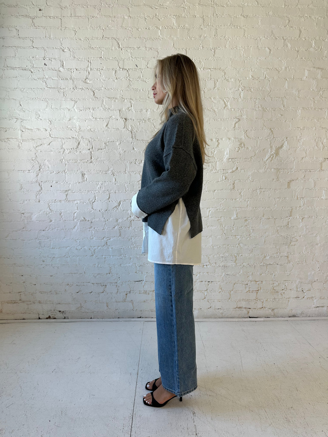 Woman wearing dark grey contrast sweater with white material sticking out the bottom.