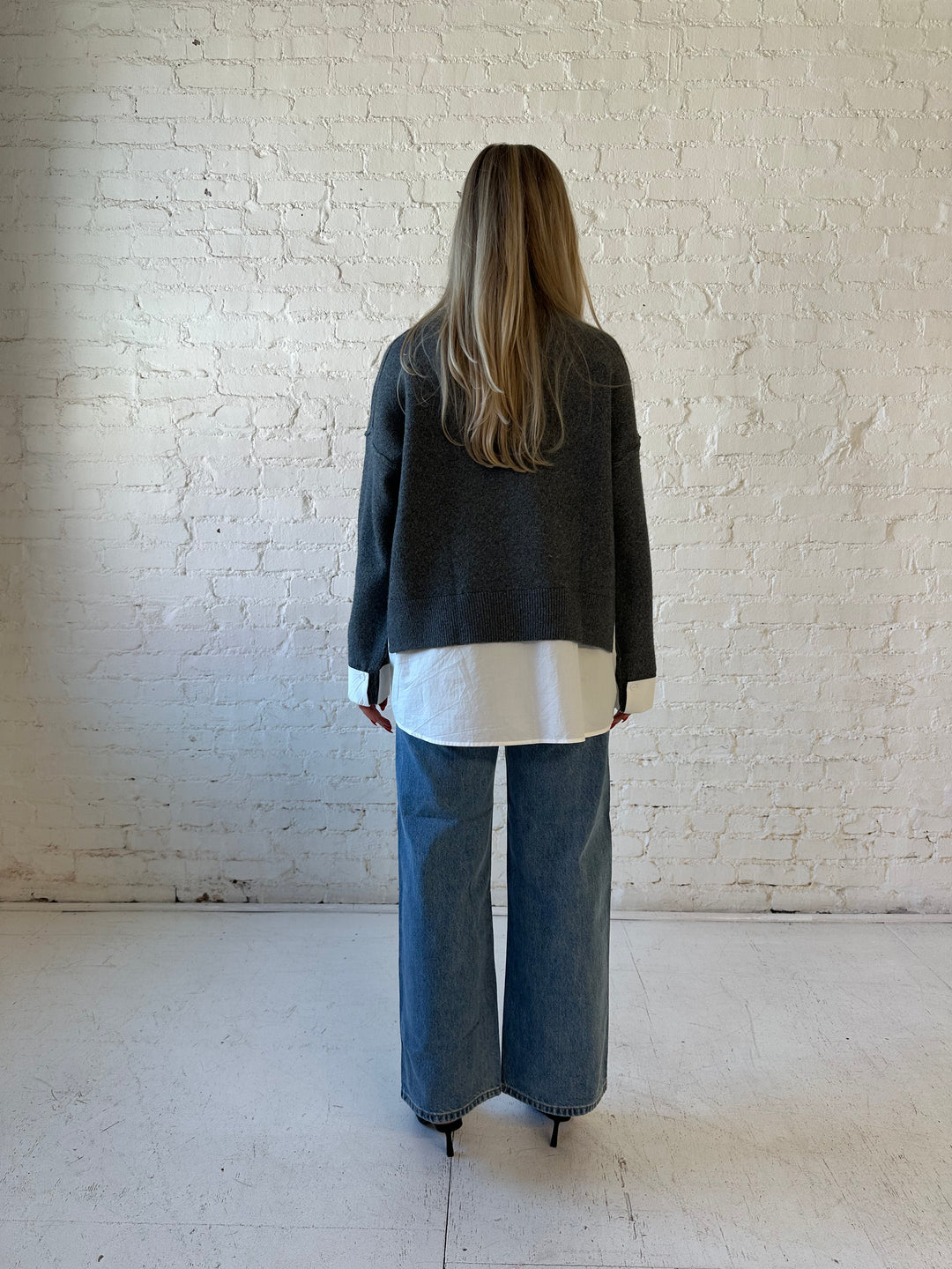 Woman wearing dark grey contrast sweater with white material sticking out the bottom.