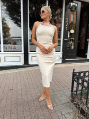 Woman wearing tan halter midi dress with gold chain link detail and slit up the back.