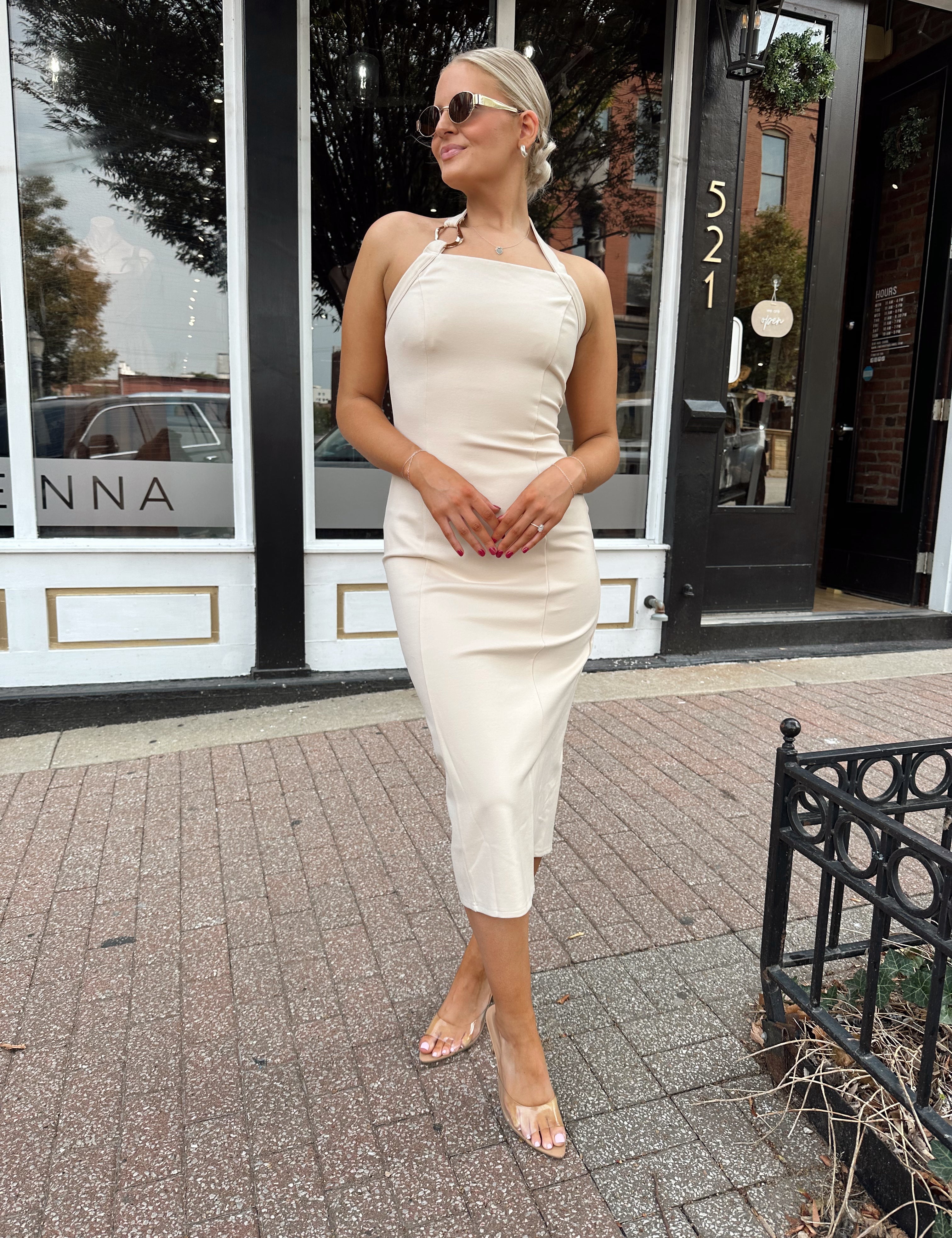 Woman wearing tan halter midi dress with gold chain link detail and slit up the back.