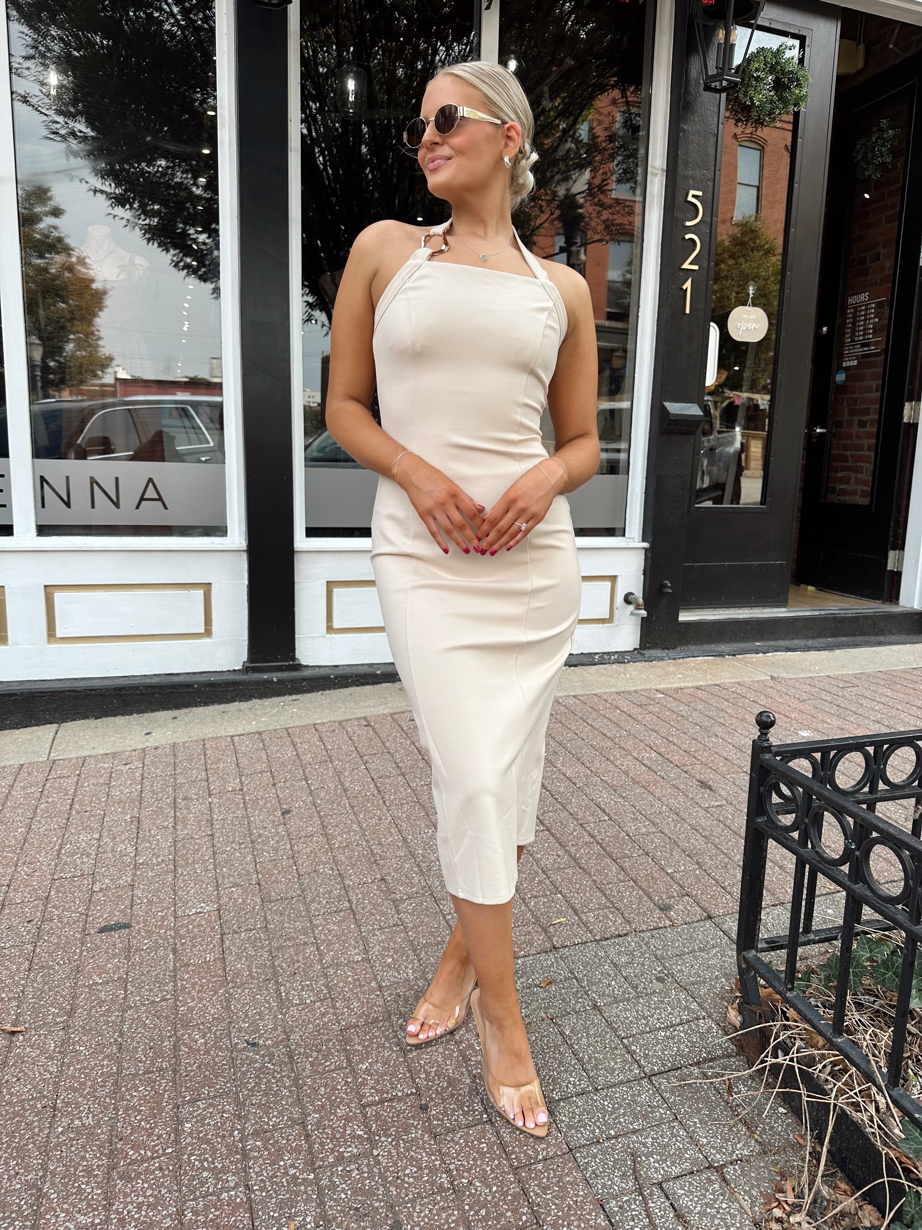Woman wearing tan halter midi dress with gold chain link detail and slit up the back.