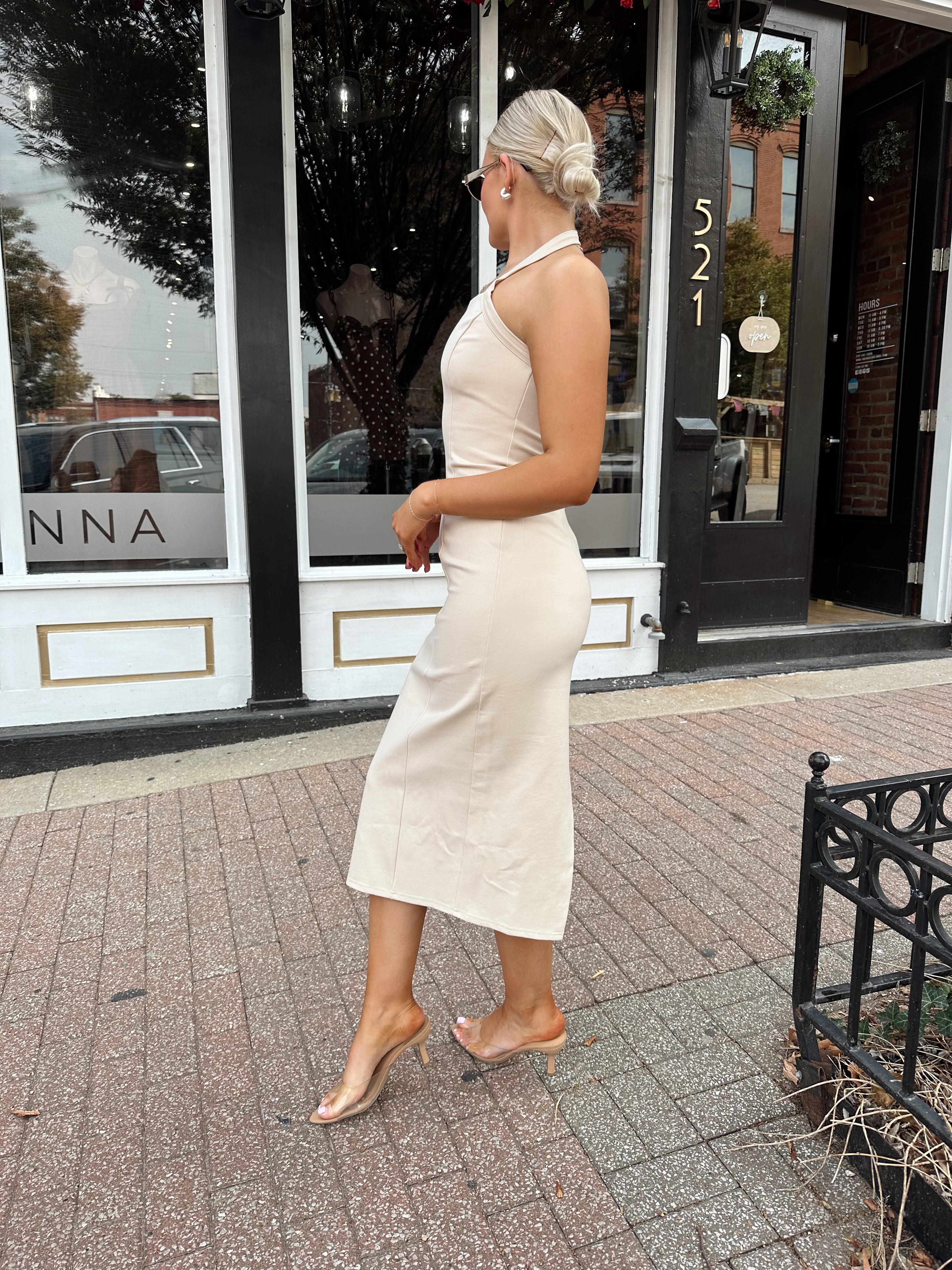 Woman wearing tan halter midi dress with gold chain link detail and slit up the back.
