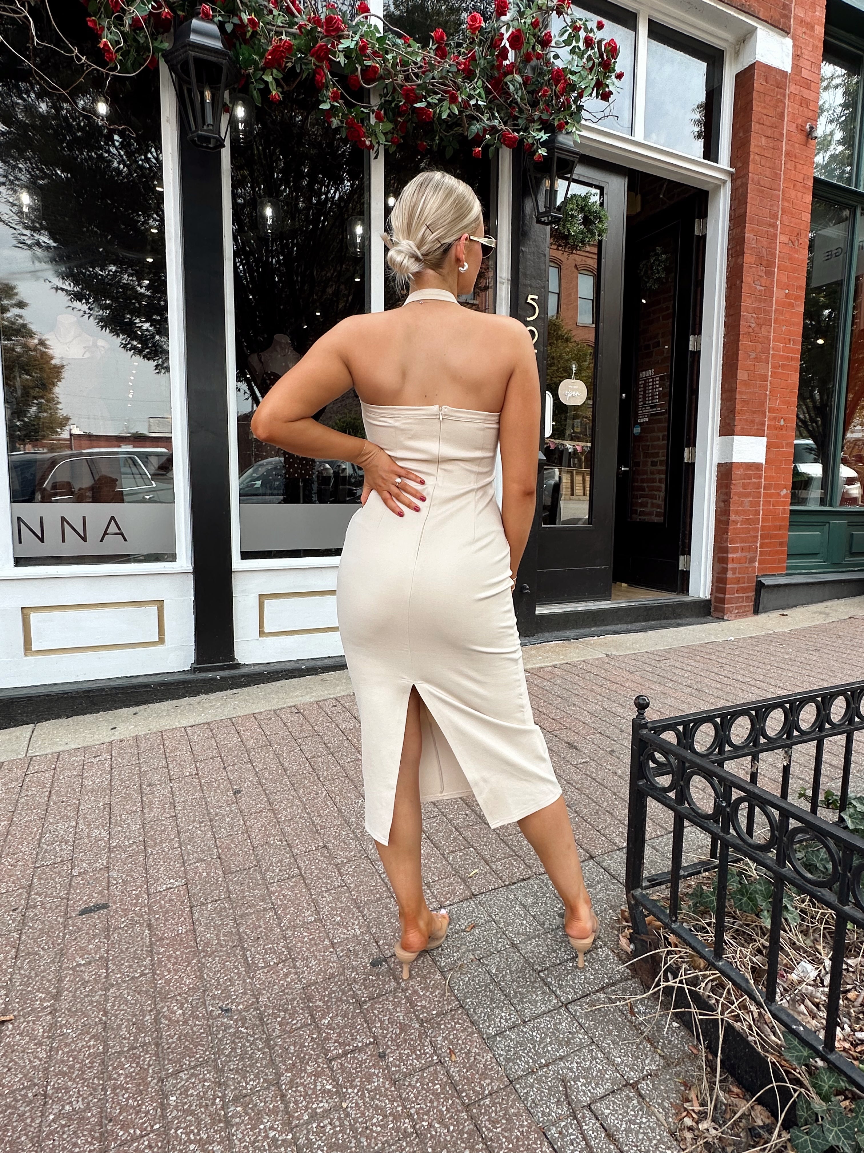 Woman wearing tan halter midi dress with gold chain link detail and slit up the back.