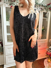 Woman wearing black tassel shift mini dress with black closed toed heel.