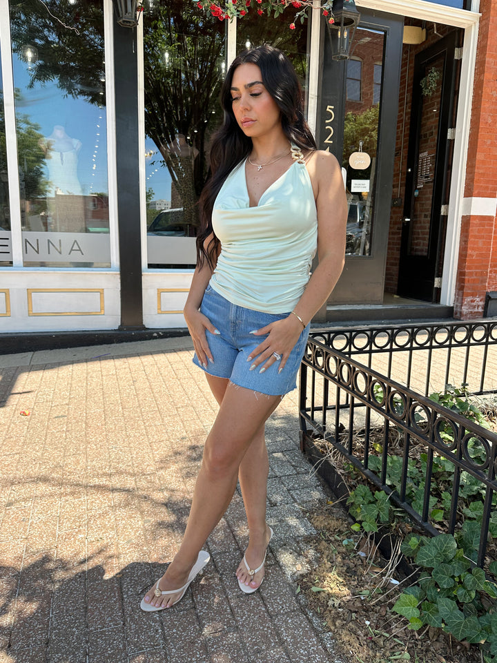 Woman wearing mint green, self tie halter top with ring detailing, ruched sides, and cowl neckline. 