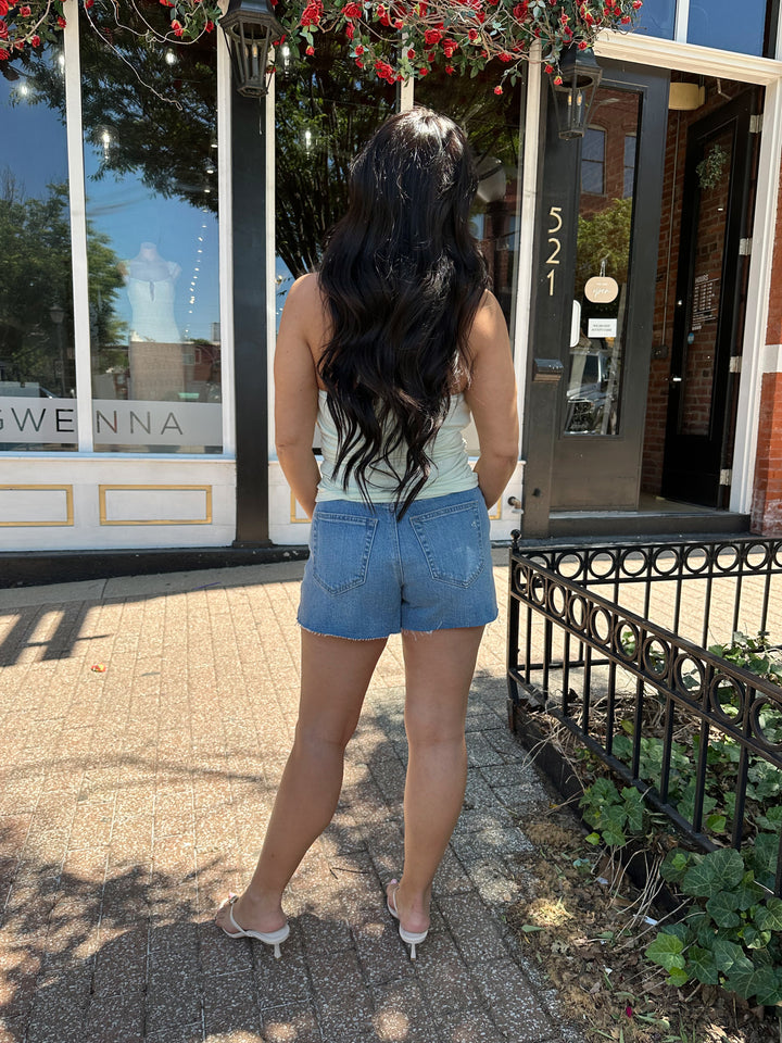 Woman wearing mint green, self tie halter top with ring detailing, ruched sides, and cowl neckline. 