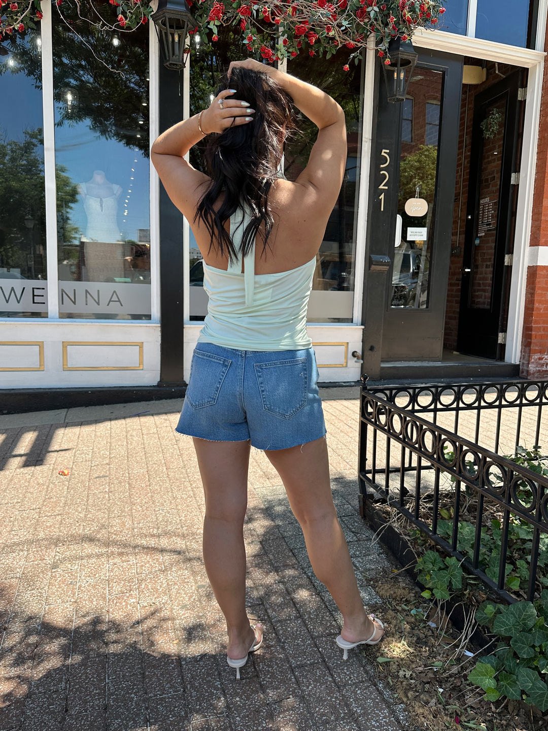 Woman wearing mint green, self tie halter top with ring detailing, ruched sides, and cowl neckline. 