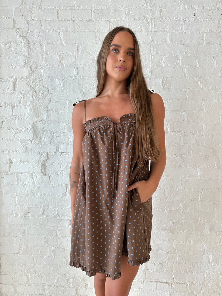 Woman wearing brown babydoll style mini dress with blue polka dots and self tie straps. 