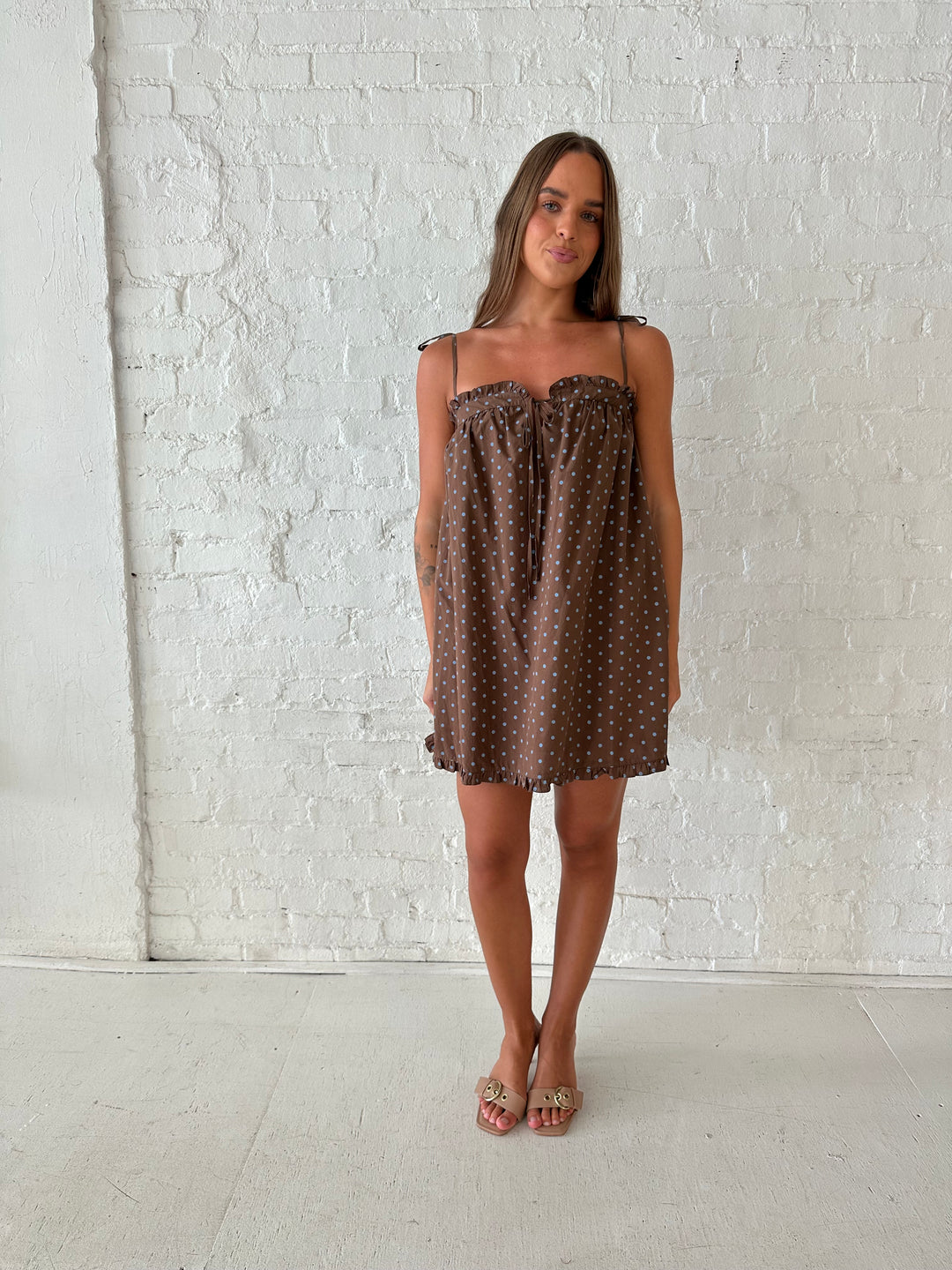 Woman wearing brown babydoll style mini dress with blue polka dots and self tie straps. 