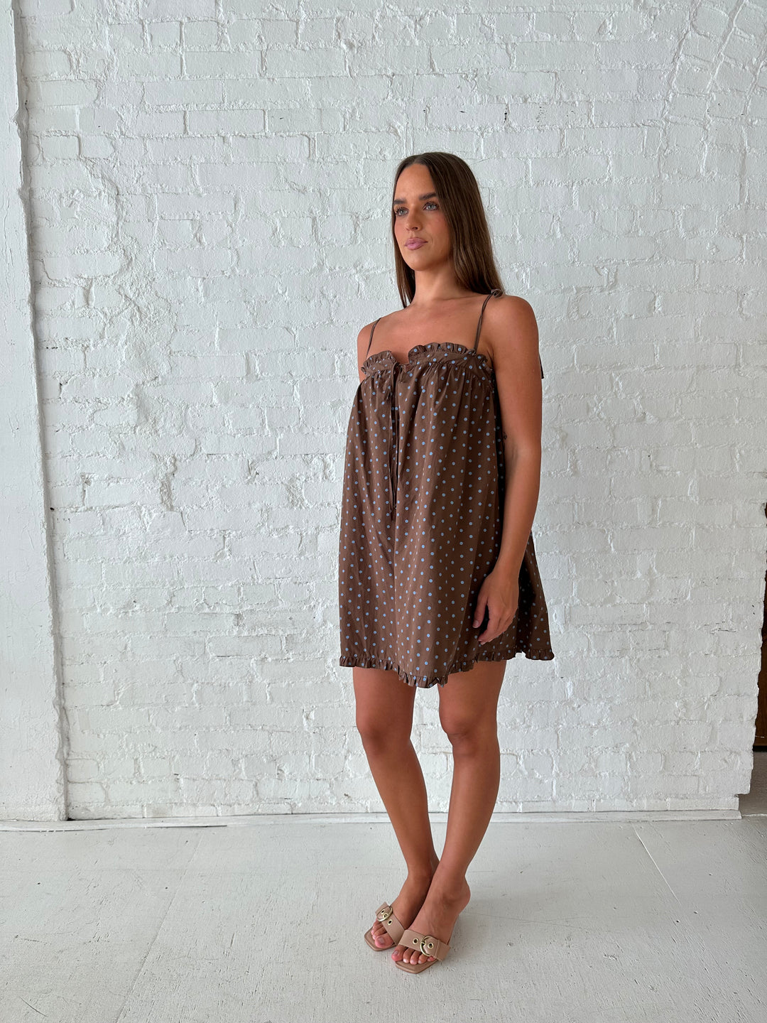 Woman wearing brown babydoll style mini dress with blue polka dots and self tie straps. 