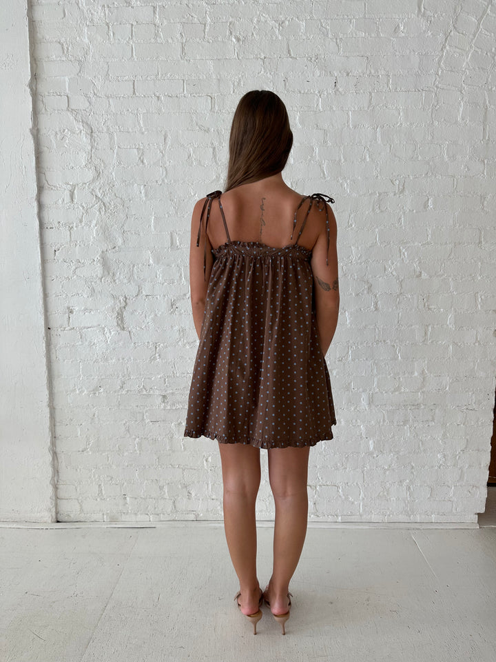 Woman wearing brown babydoll style mini dress with blue polka dots and self tie straps. 