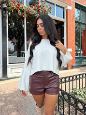 Woman wearing burgundy leather short with functional pockets and white top.