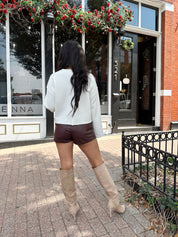 Woman wearing burgundy leather short with functional pockets and white top.