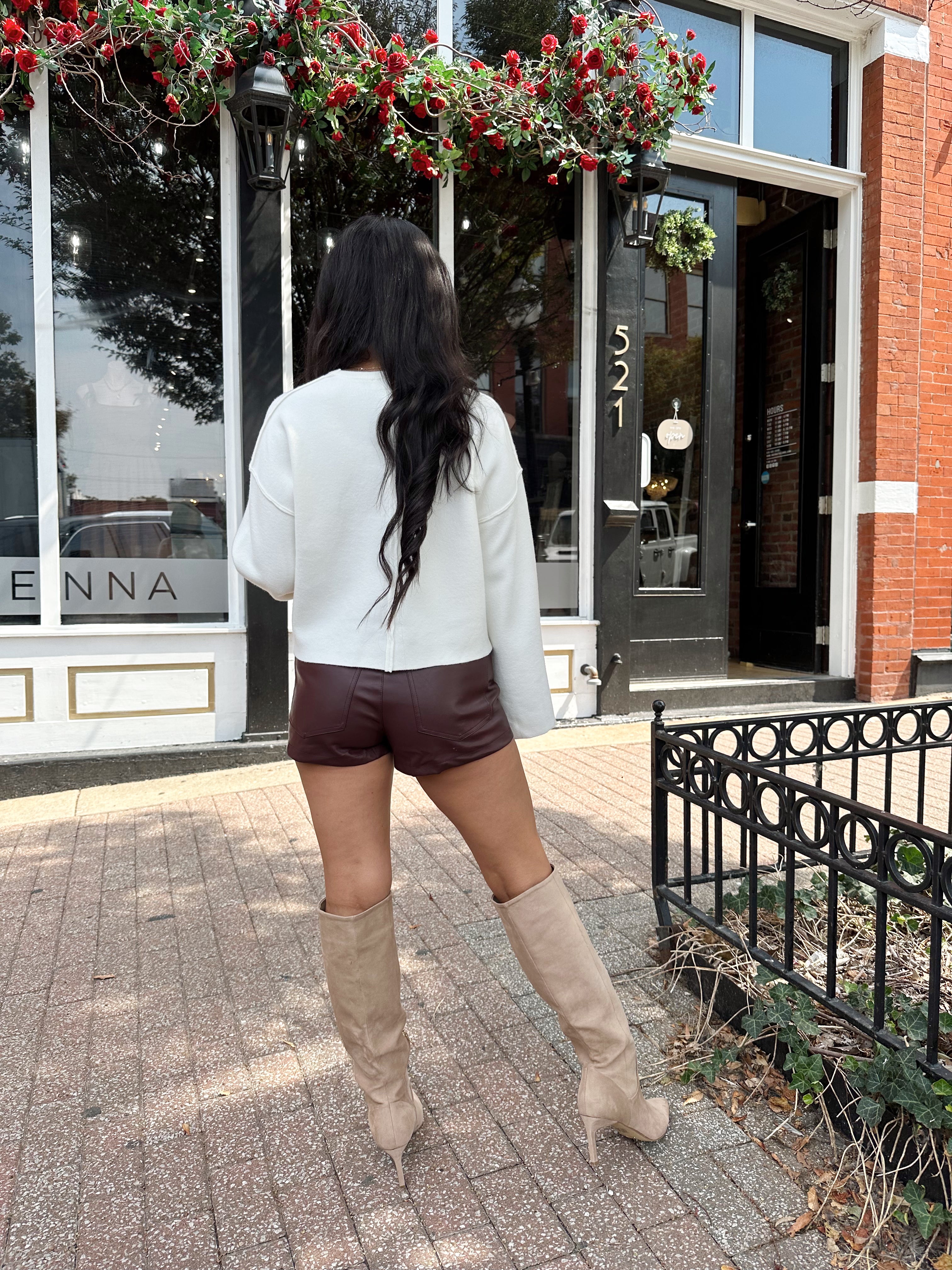 Woman wearing burgundy leather short with functional pockets and white top.