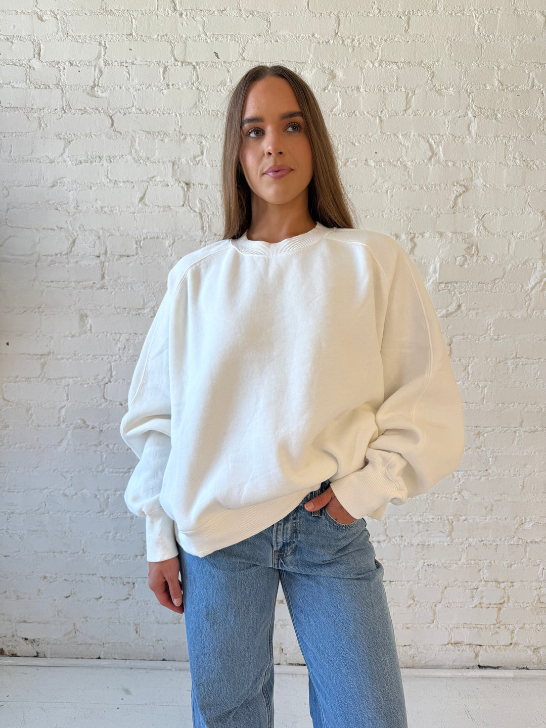 Woman wearing over sized off white crew neck sweatshirt with medium wash jeans. 