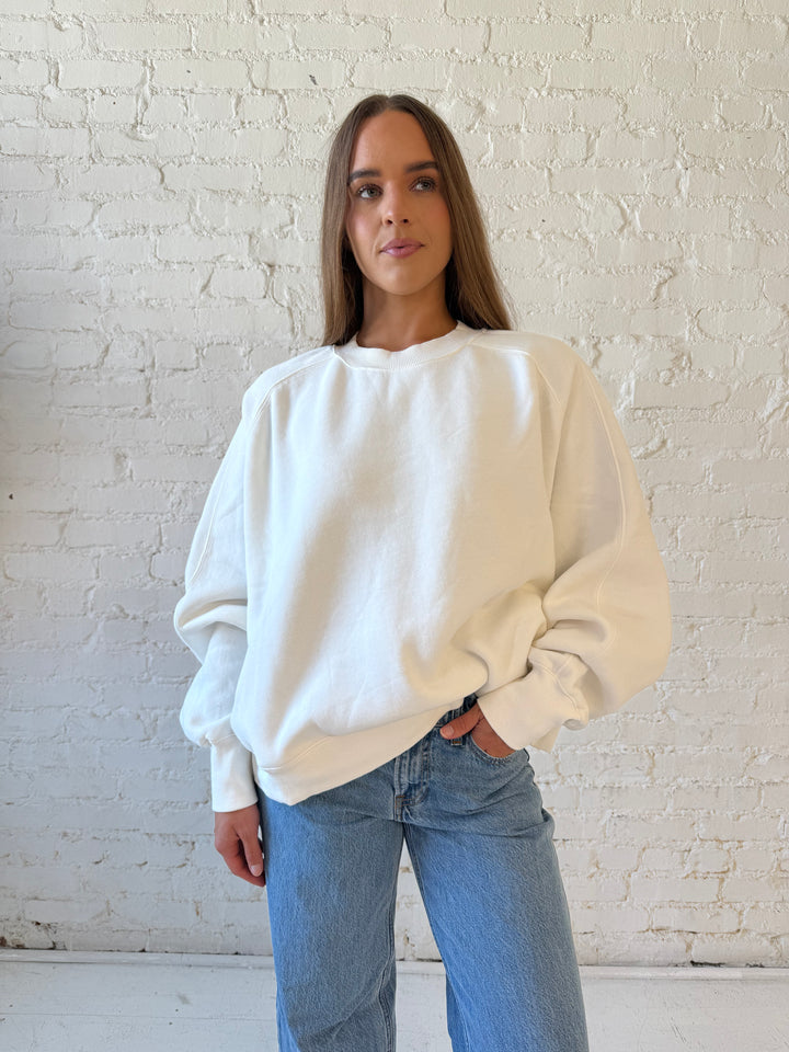 Woman wearing over sized off white crew neck sweatshirt with medium wash jeans. 