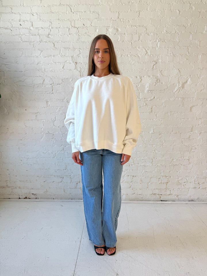 Woman wearing over sized off white crew neck sweatshirt with medium wash jeans. 